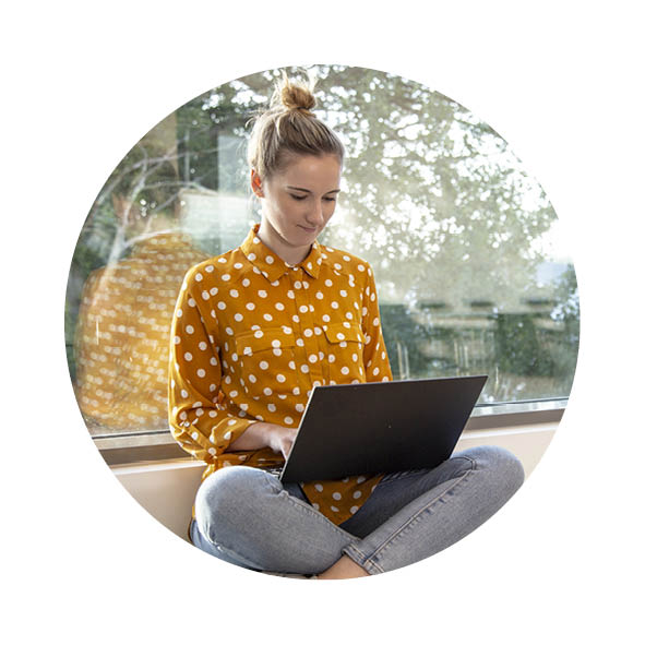 eine Frau sitzt auf einer Fensterbank und hat einen Laptop auf dem Schoß und arbeitet