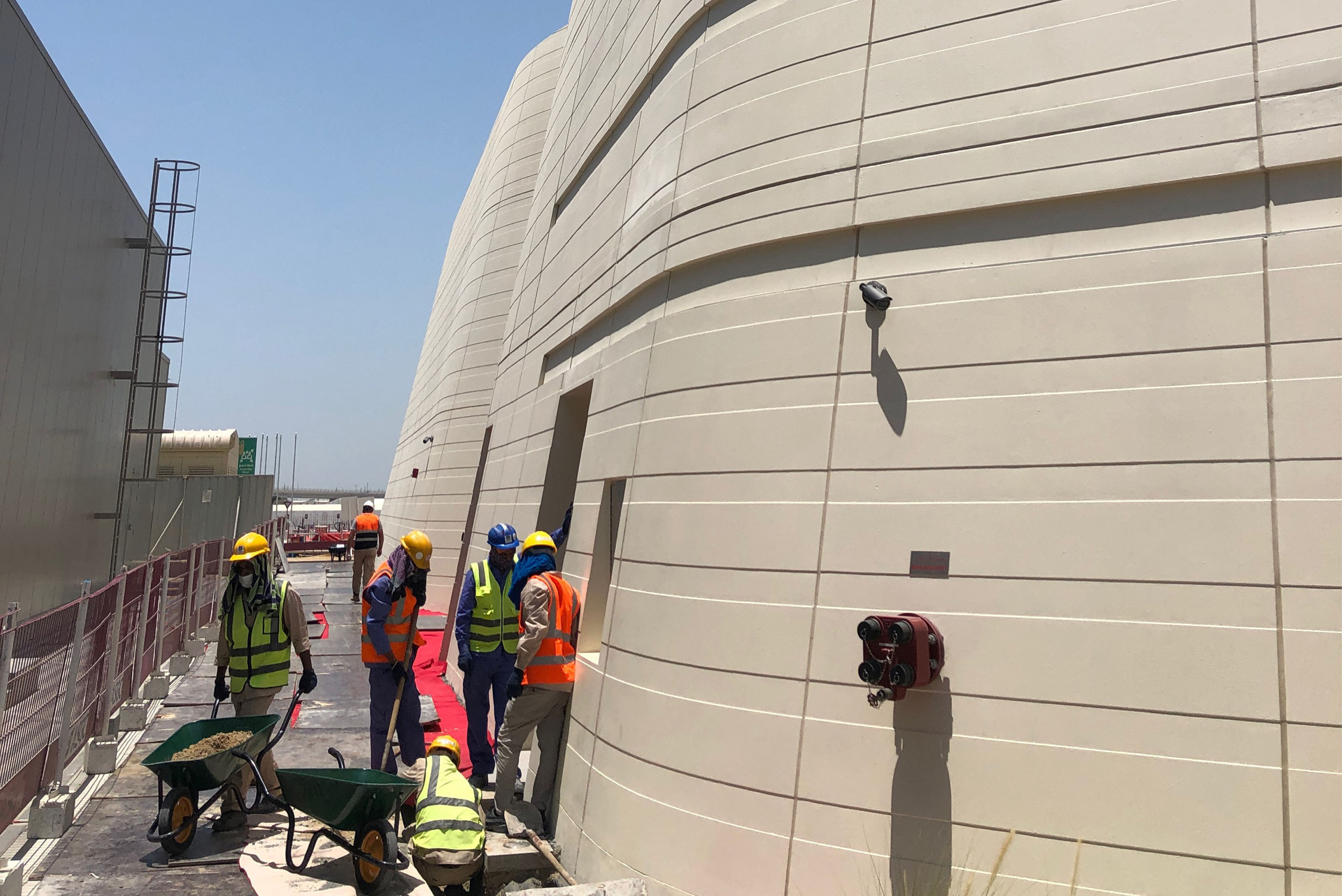 mehrere Männer in Arbeitskleidung  auf einer Baustelle neben einem beigen Gebäude