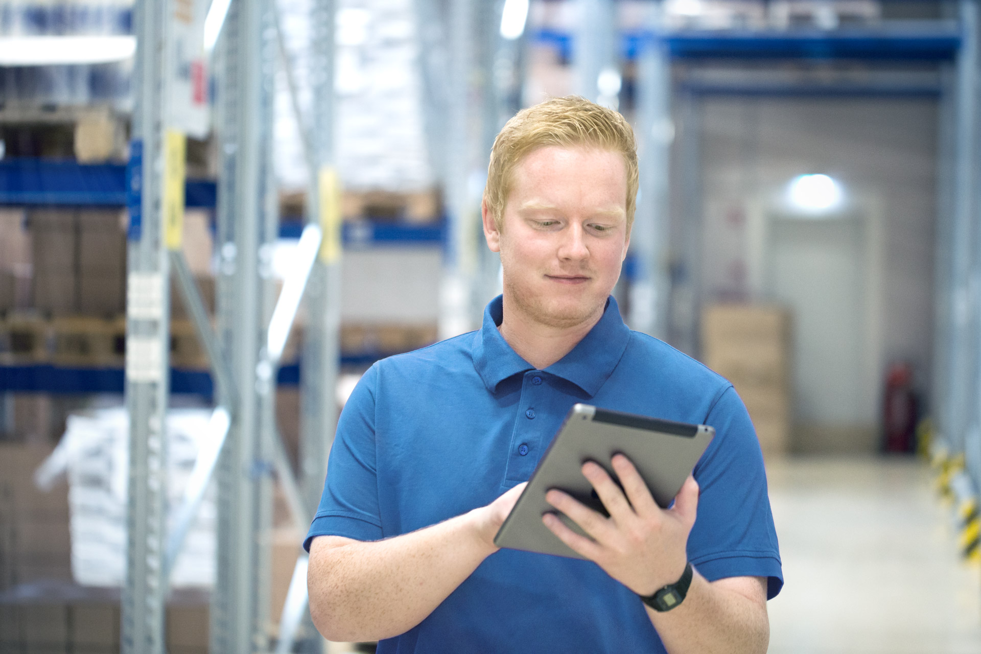 digitalisierung-arbeitsprozesse-weicon Ein Mann mit blauem T-Shirt steht in einem Lager, hält ein Tablet in der Hand und tippt mit der anderen Hand darauf
