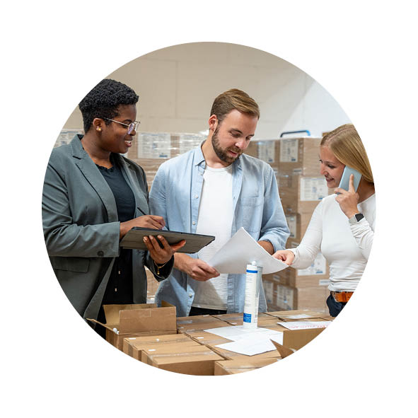 Zwei Frauen und ein Mann stehen in einem Lager und checken Papiere, eine Frau telefoniert