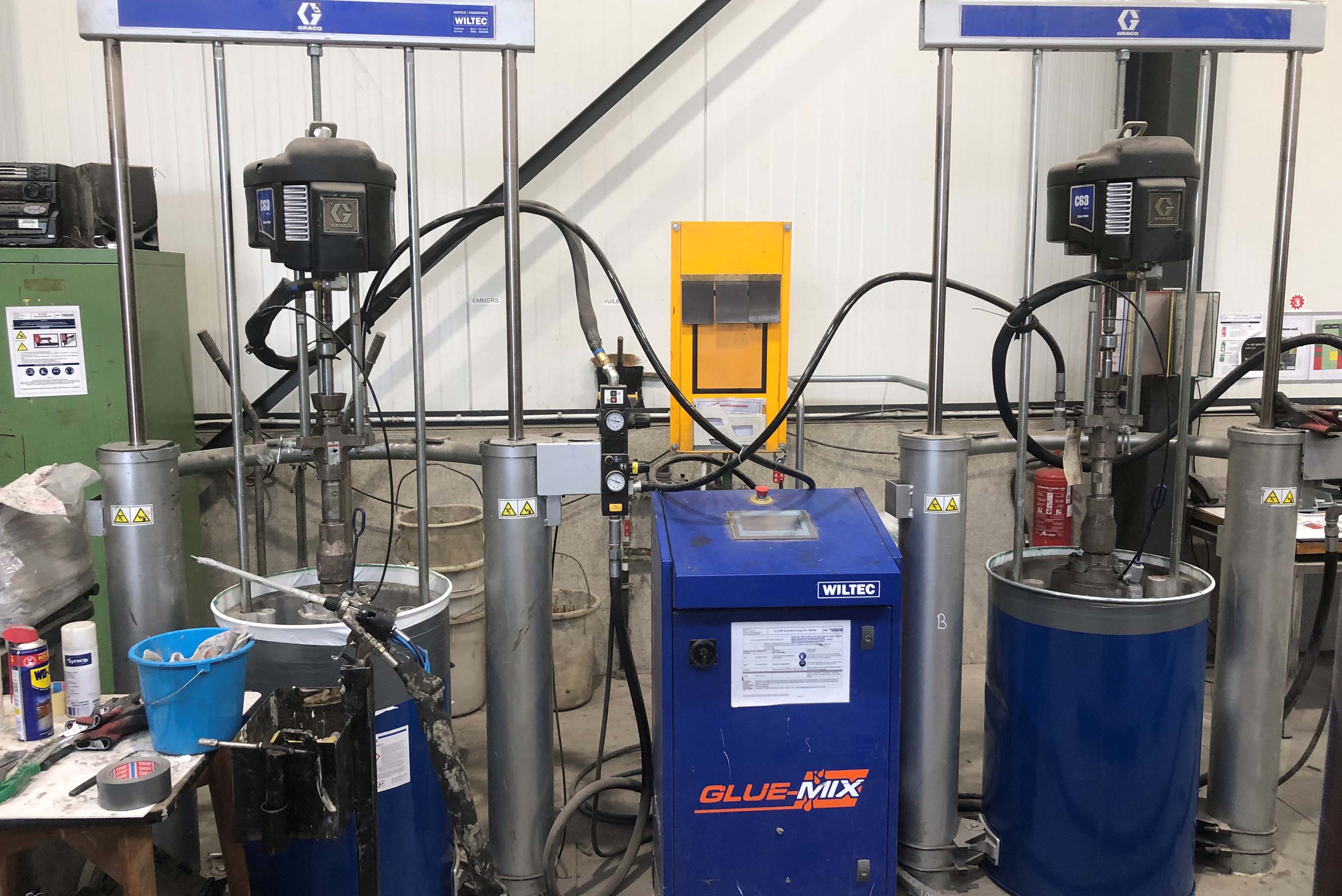 Eine industrielle Umgebung mit zwei Klebstoffmischmaschinen, die mit “GLUE MIX” beschriftet sind