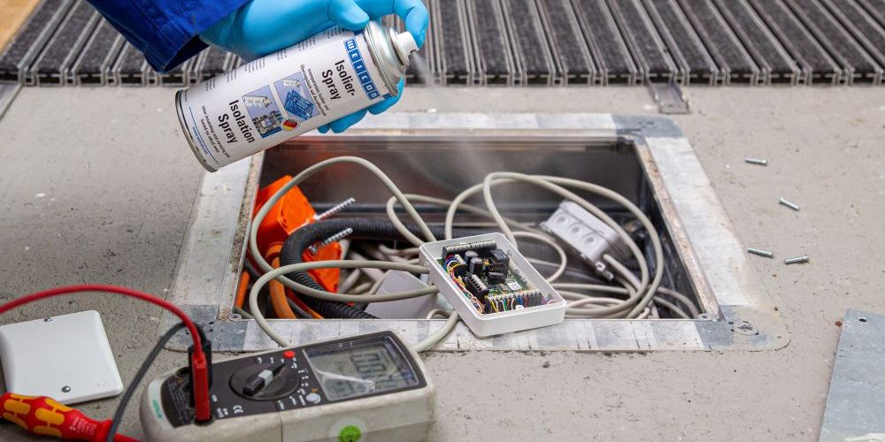 In Boden gelegter Kasten mit Kabeln wird mit Isolier-Spray besprüht