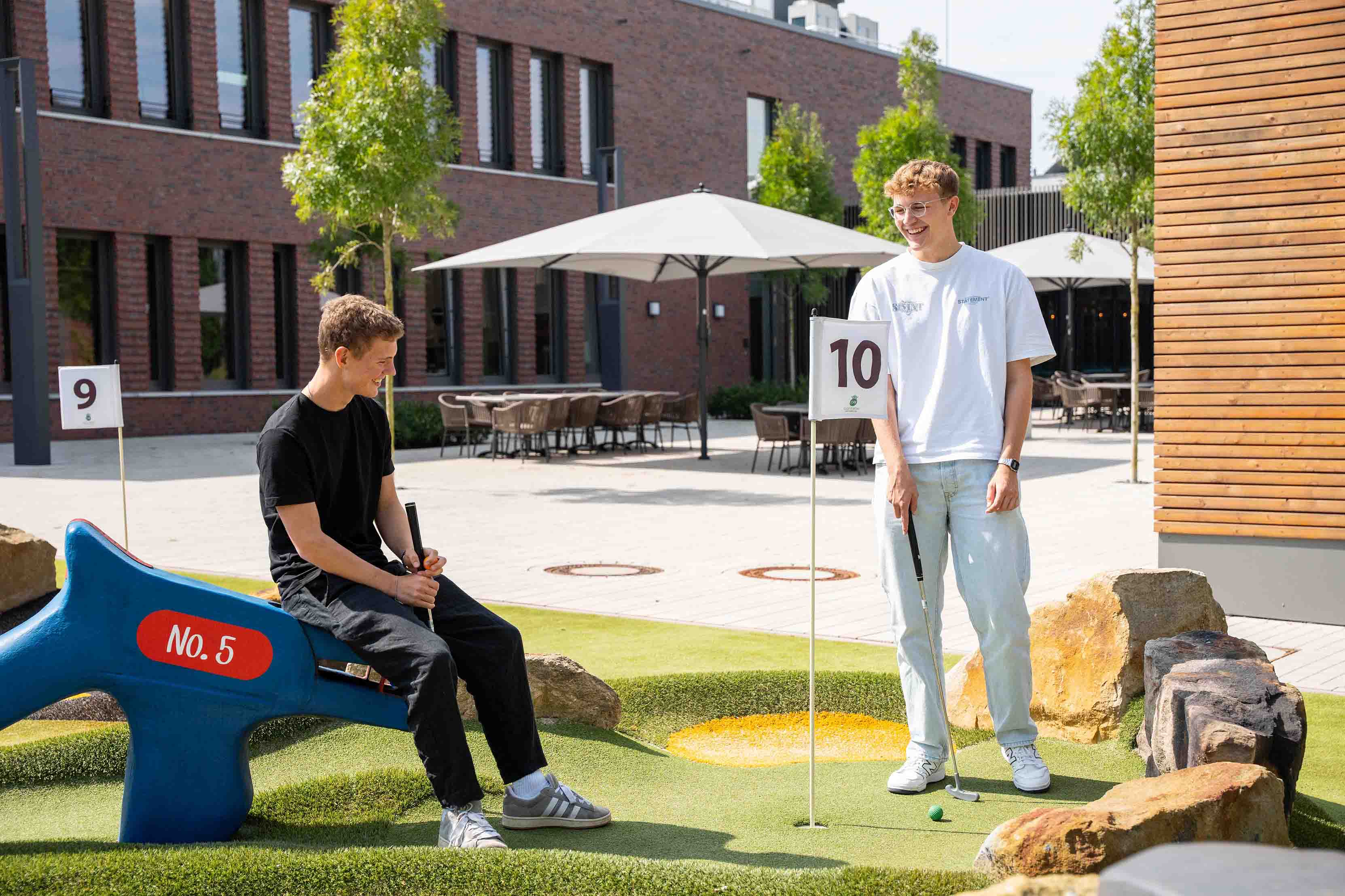 Zwei junge Männer spielen zusammen Minigolf und lachen dabei.