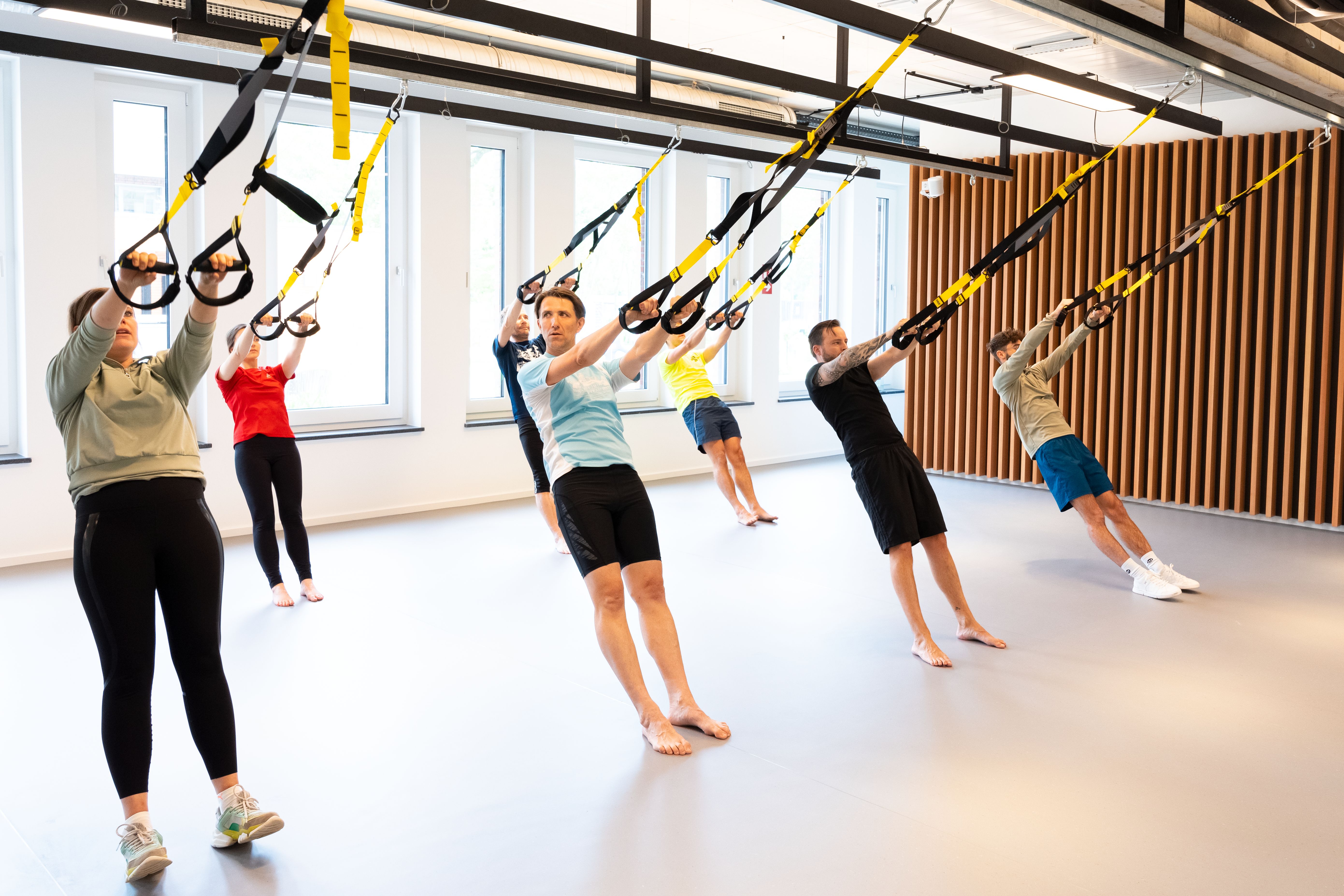 Mehrere Menschen sind in einem Sportraum und arbeiten mit TRX-Bändern
