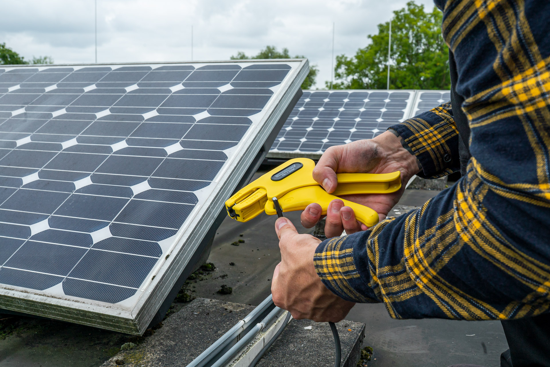 solarenergie-weicon jemand ist auch einem Dach auf dem Solarpanele angebracht sind, er hält eine Abisolierzange für Solarkabel in der Hand