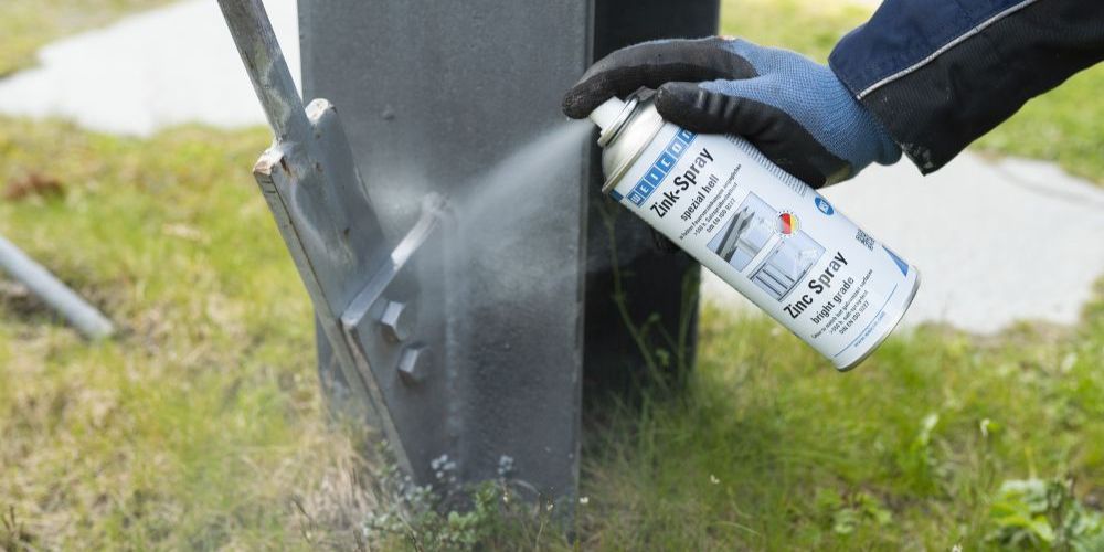 Helles Zinkspray wird auf Metallträger gesprüht